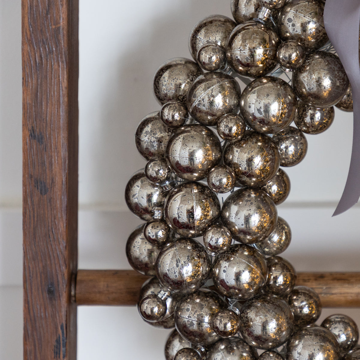 Decorative wreath with metallic balls on a wooden frame against a white wall.