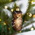Decorative owl ornament hanging on a Christmas tree with lights in the background.