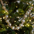 A strand of large, reflective silver glass beads wrapped on a rustic twine, draped over green pine tree branches with warm white string lights.