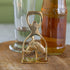 A gold-finished metal bottle opener shaped like a horse head, standing on a wooden surface with a glass and an amber bottle in the background.