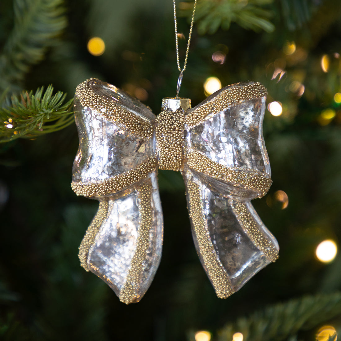 Antique Silver Bow with Gold Beading Ornament on a Christmas tree with blurred lights in the background.