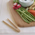 Wooden cutting board with green beans, carrots, radishes, and a bowl of dip on a light surface.