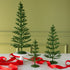Three decorative green tinsel trees on a table with red ribbons against a green wall.