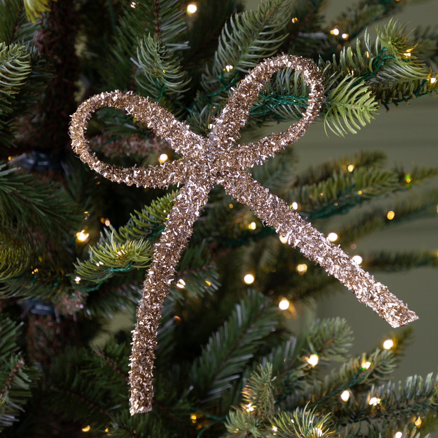 Decorative gold glitter bow ornament on a Christmas tree with lights.