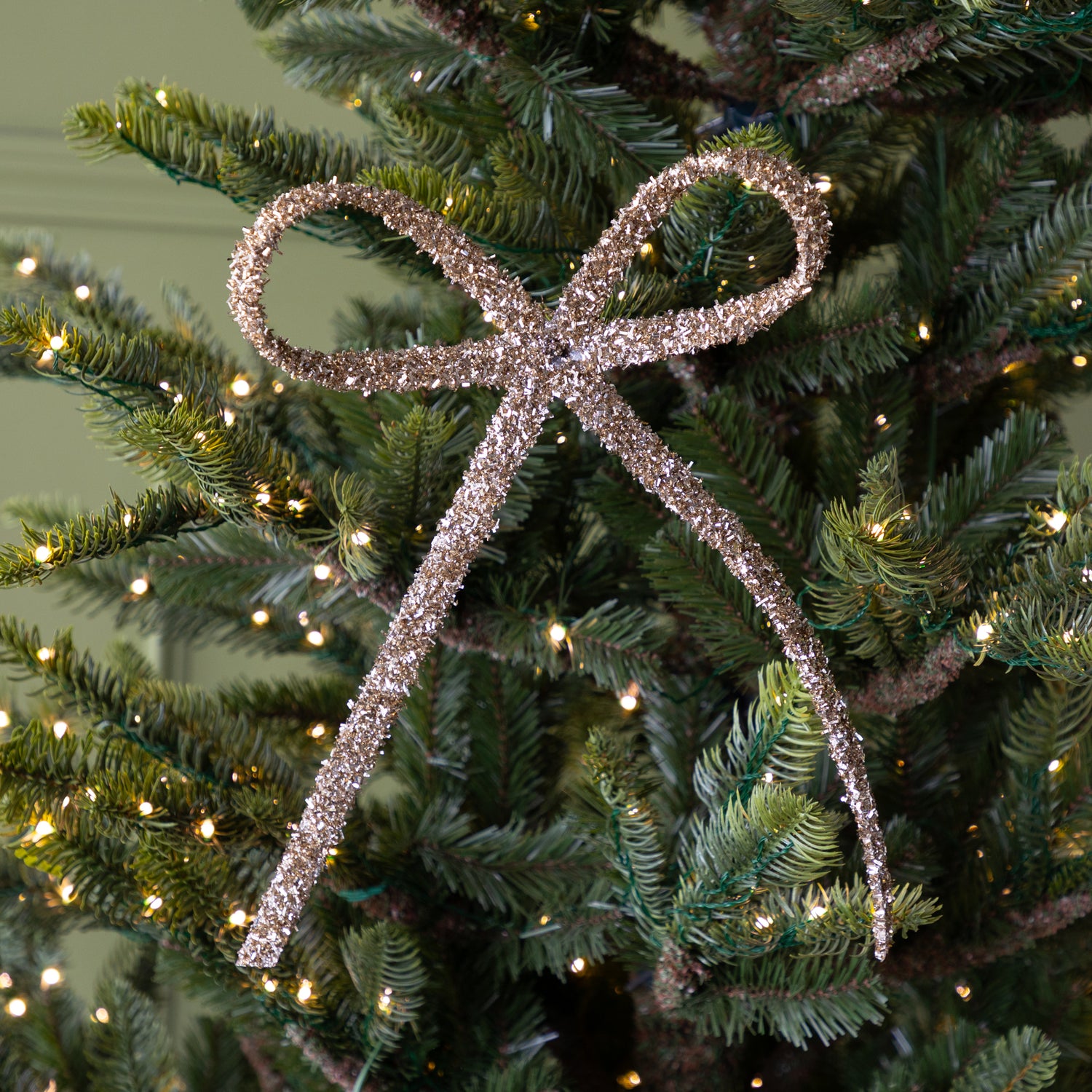 Decorative gold glitter bow ornament on a Christmas tree with lights.