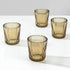 Four amber-tinted glass tumblers with a ribbed fluted design, arranged on a white reflective surface against a light gray background.