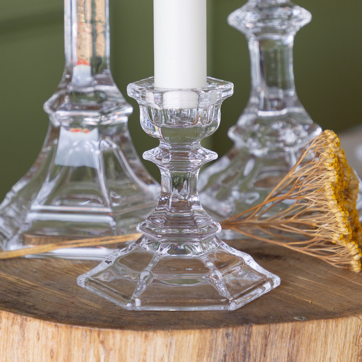 Clear glass candle holder with a white candle on a wooden surface with a blurred background.