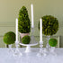 Decorative arrangement with green spherical topiaries and white candles on a marble surface.