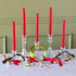 Red candles in glass candlesticks with decorative ribbons and ornaments on a marble surface.