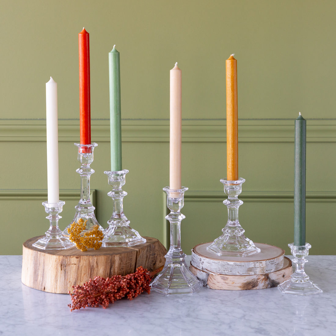 Set of colorful candles in various glass holders on a marble surface with a green background.