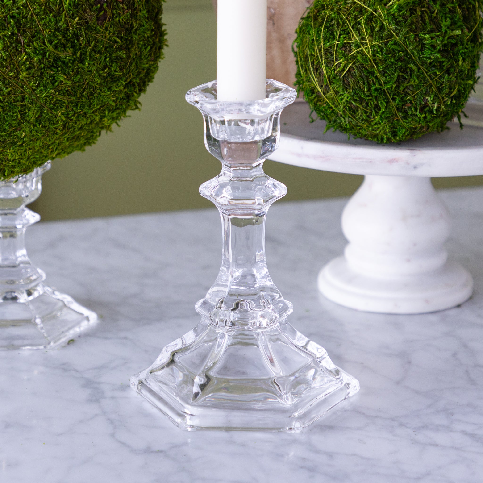 Clear glass candlestick with decorative elements on a marble surface.