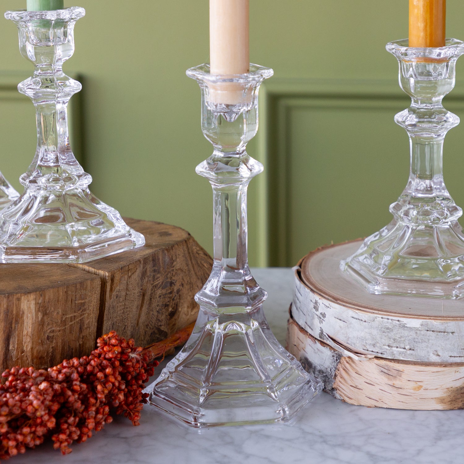 Clear glass candlesticks on wooden and marble surfaces with candles inside.