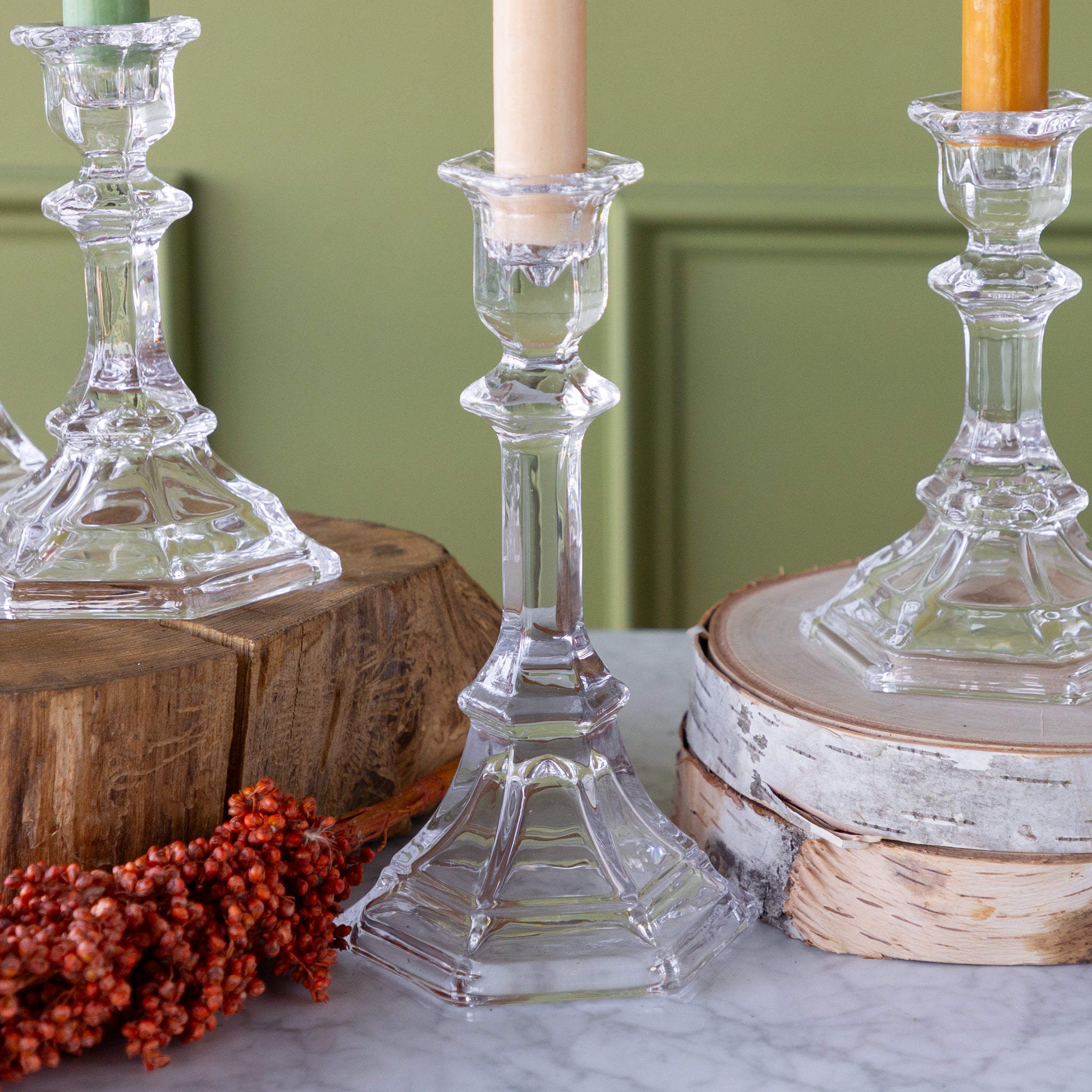 Clear glass candlesticks on wooden and marble surfaces with candles inside.