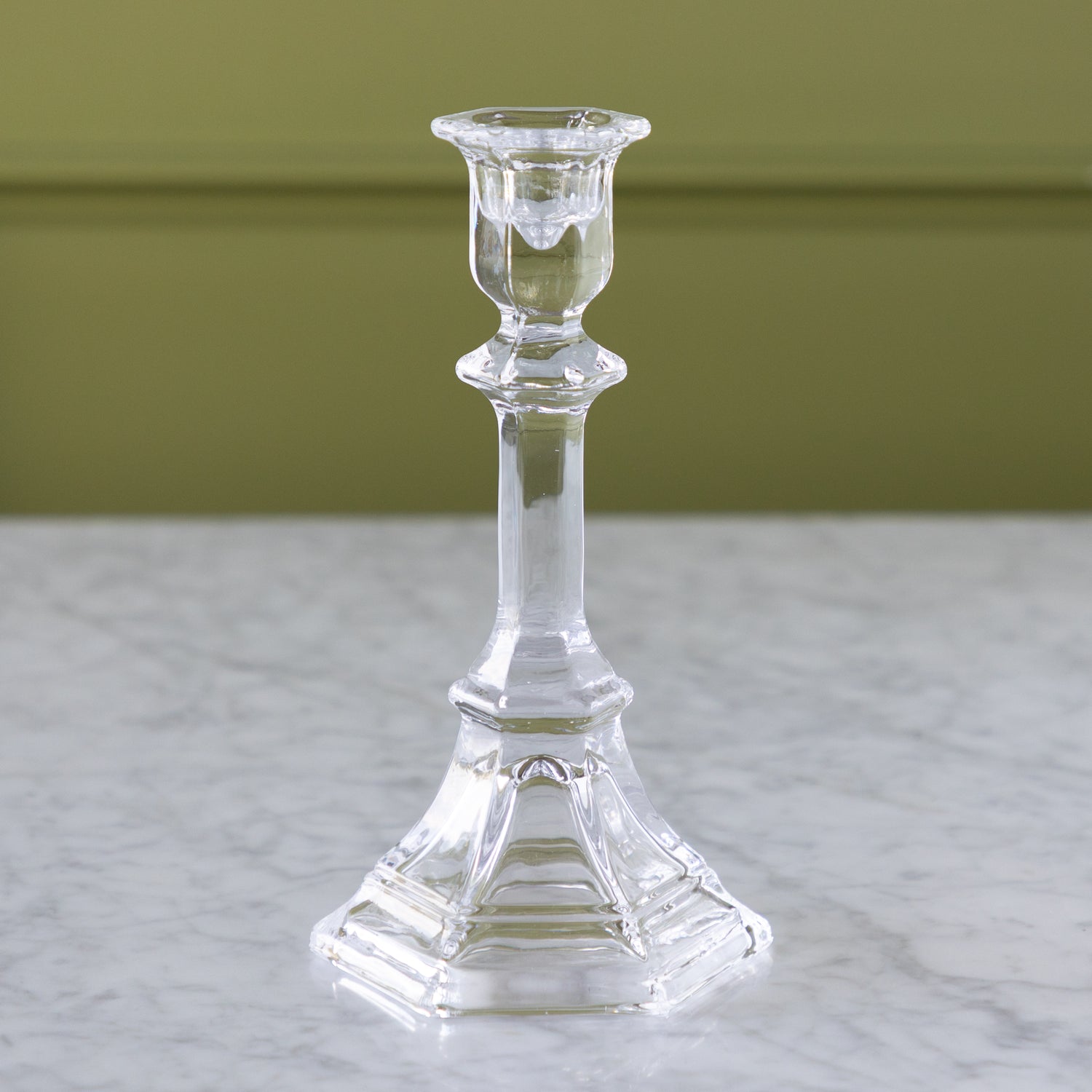 Clear glass candlestick on a marble surface with a green background.