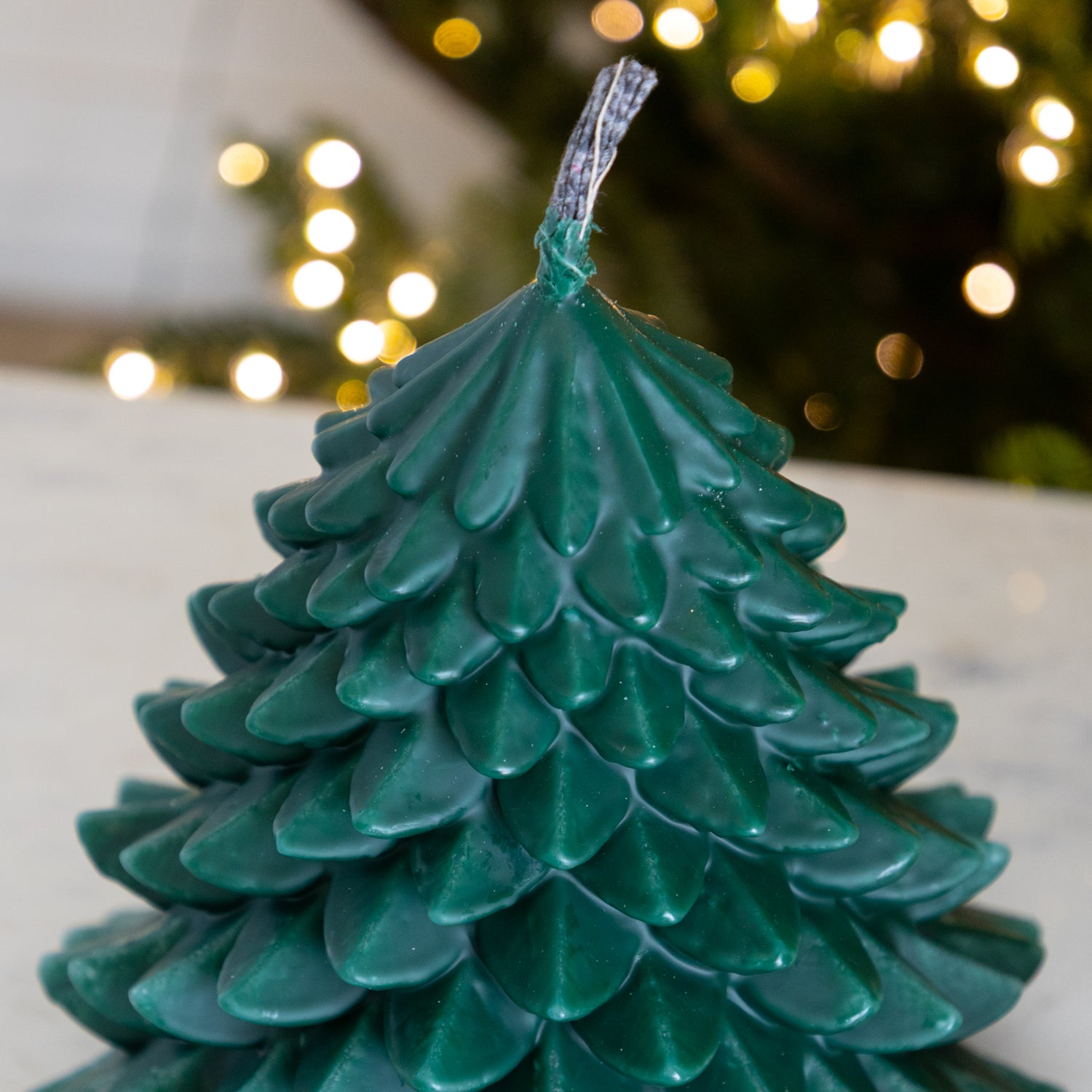 Green candle shaped like a Christmas tree with blurred lights in the background.
