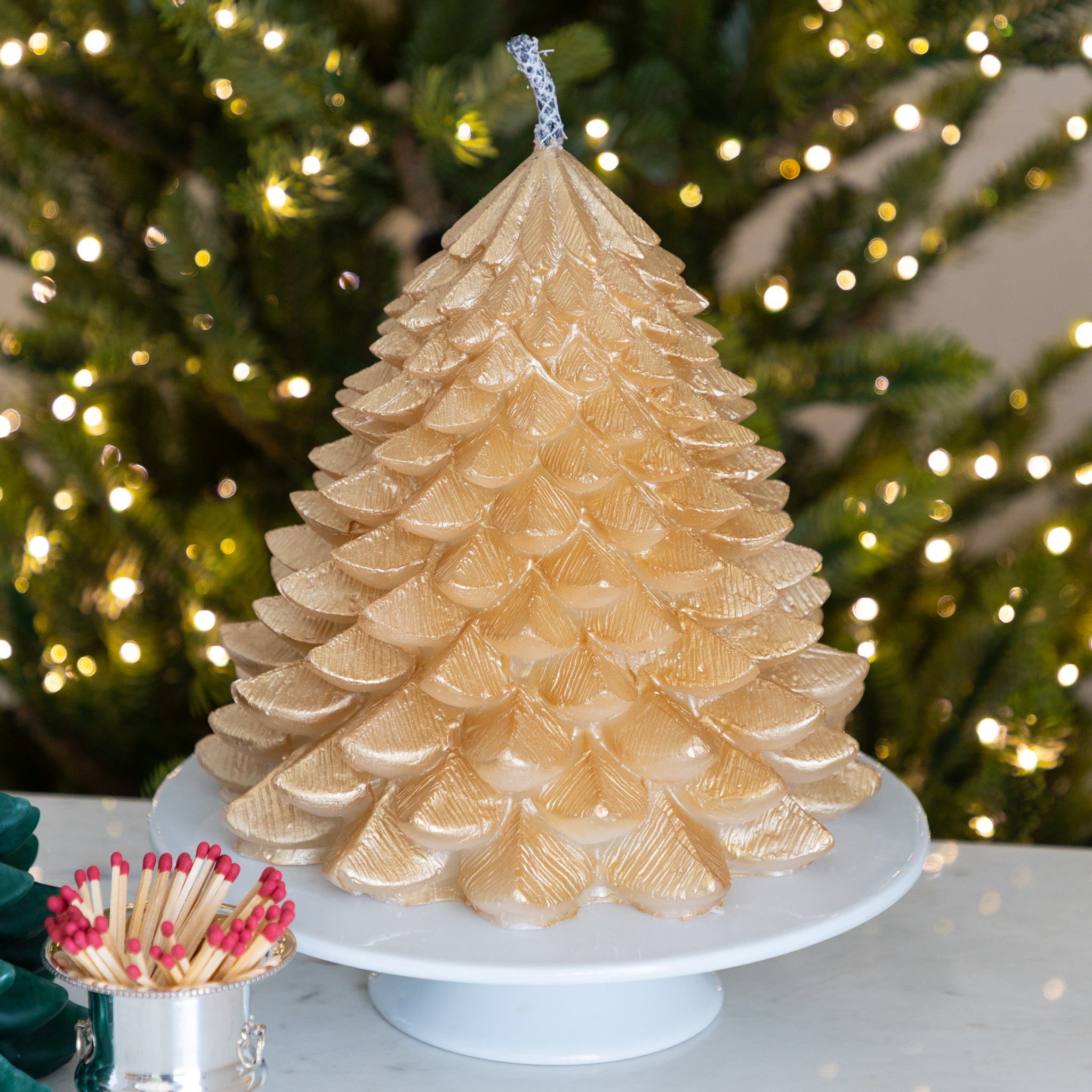 Gold candle shaped like a Christmas tree with blurred lights in the background.