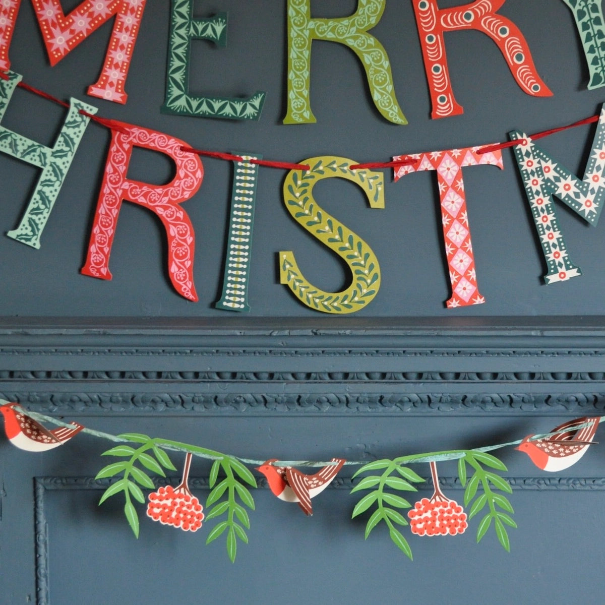 Festive paper garlands hanging on a dark teal wall. 