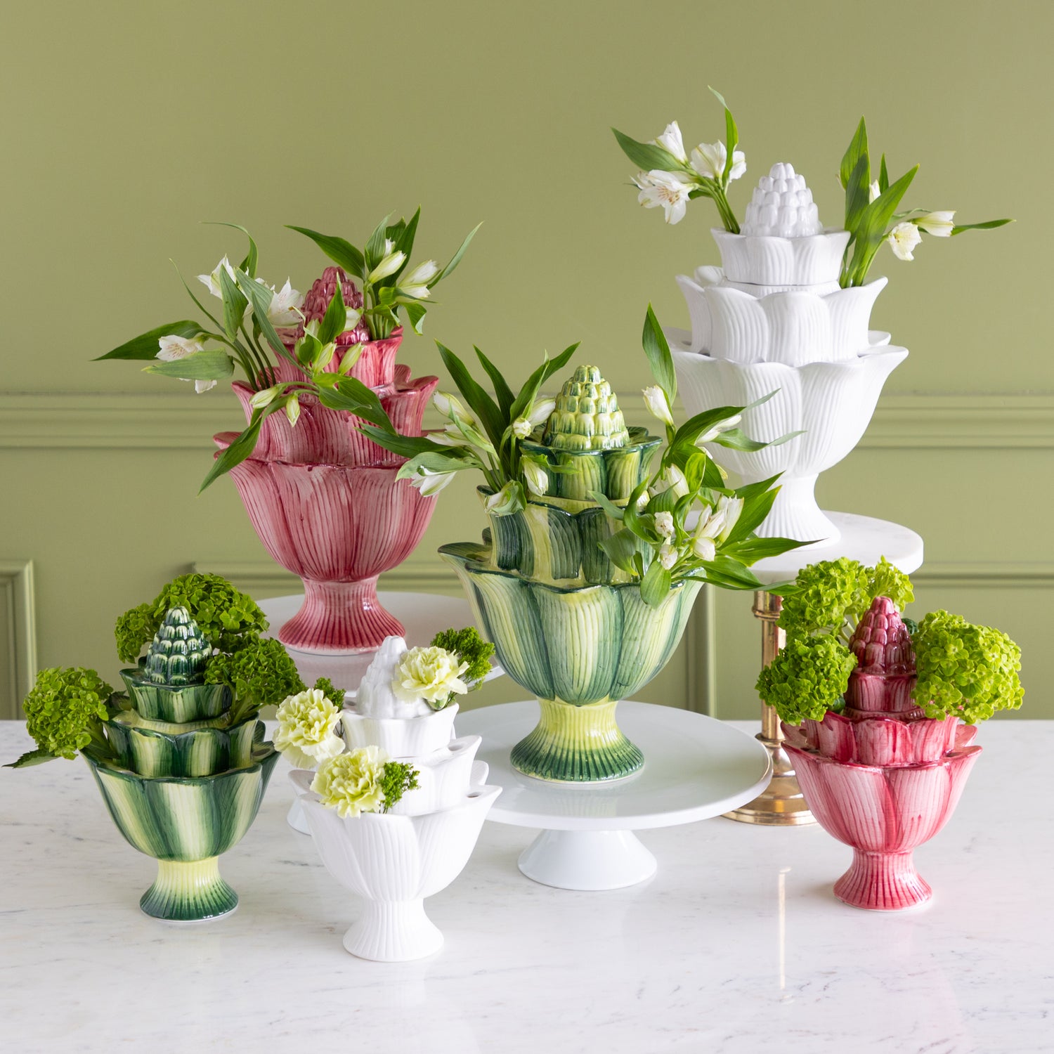 Decorative table setting with colorful vases and floral arrangements against a green wall.