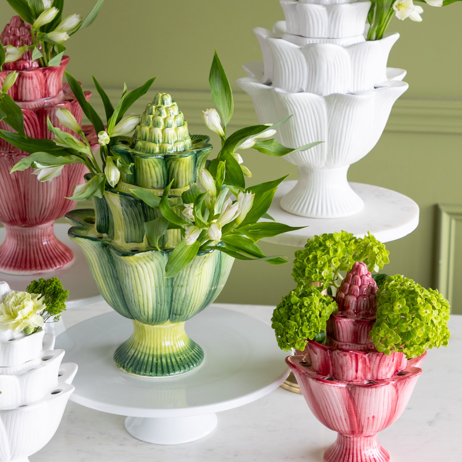 Decorative vases with floral arrangements on a white surface against a green wall.