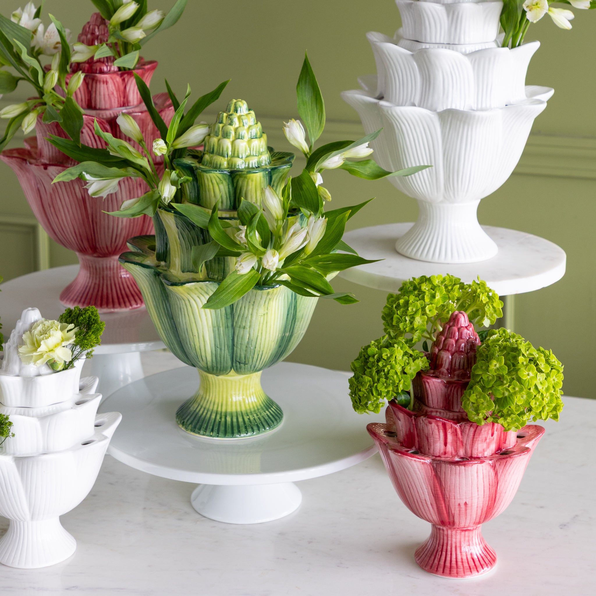 Decorative vases with floral arrangements on a white surface against a green wall.