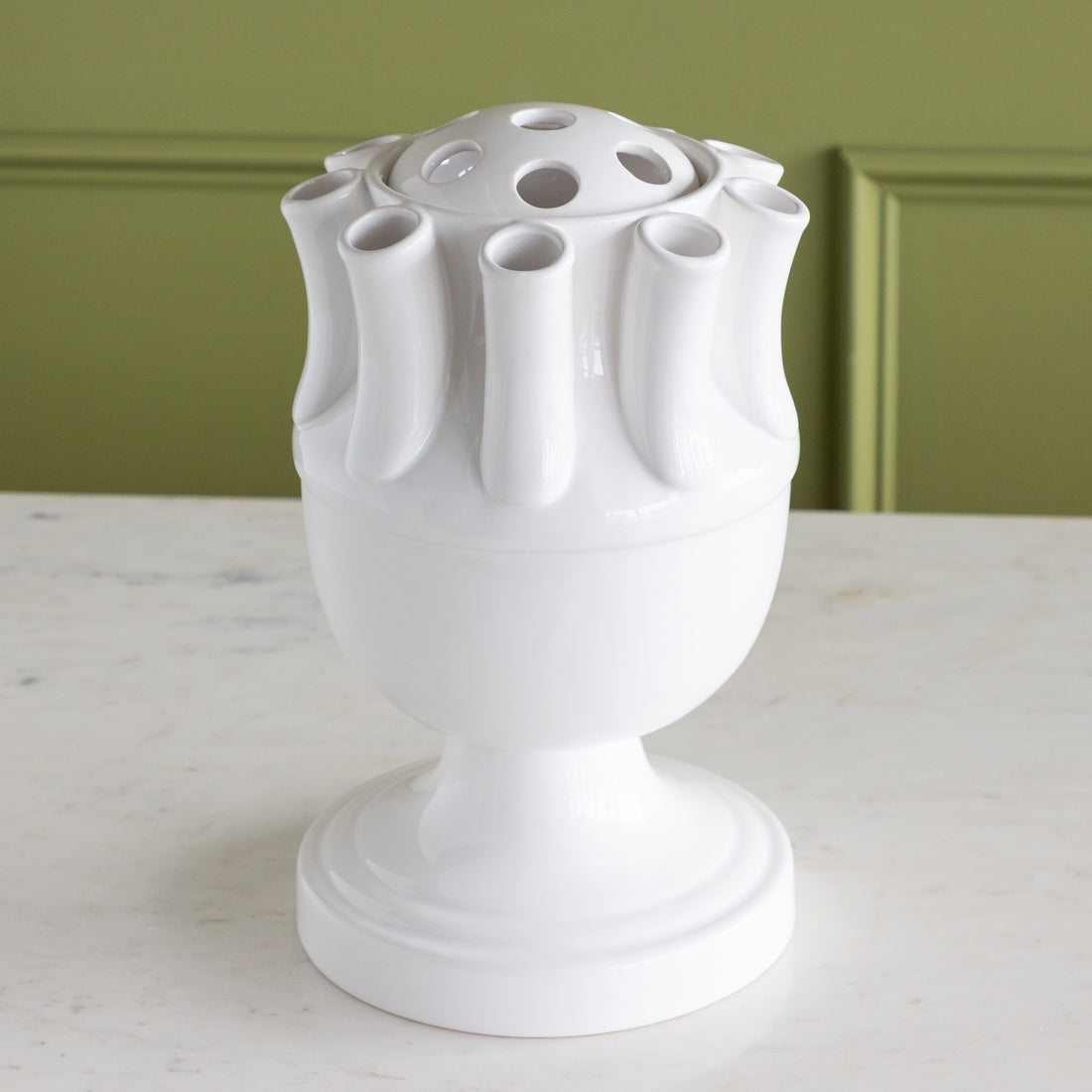 White ceramic vase with unique design on a marble surface against a green wall.