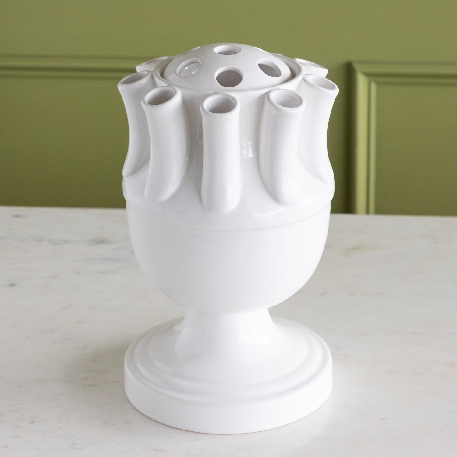White ceramic vase with unique design on a marble surface against a green wall.