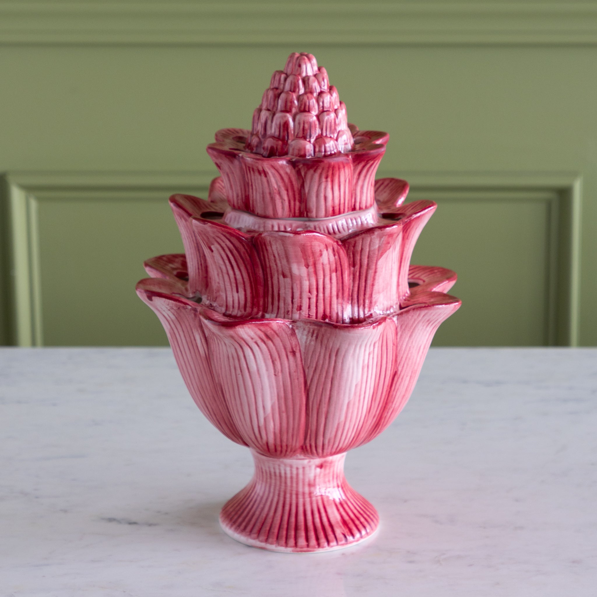 Pink ceramic water fountain on a marble surface with a green panel background.
