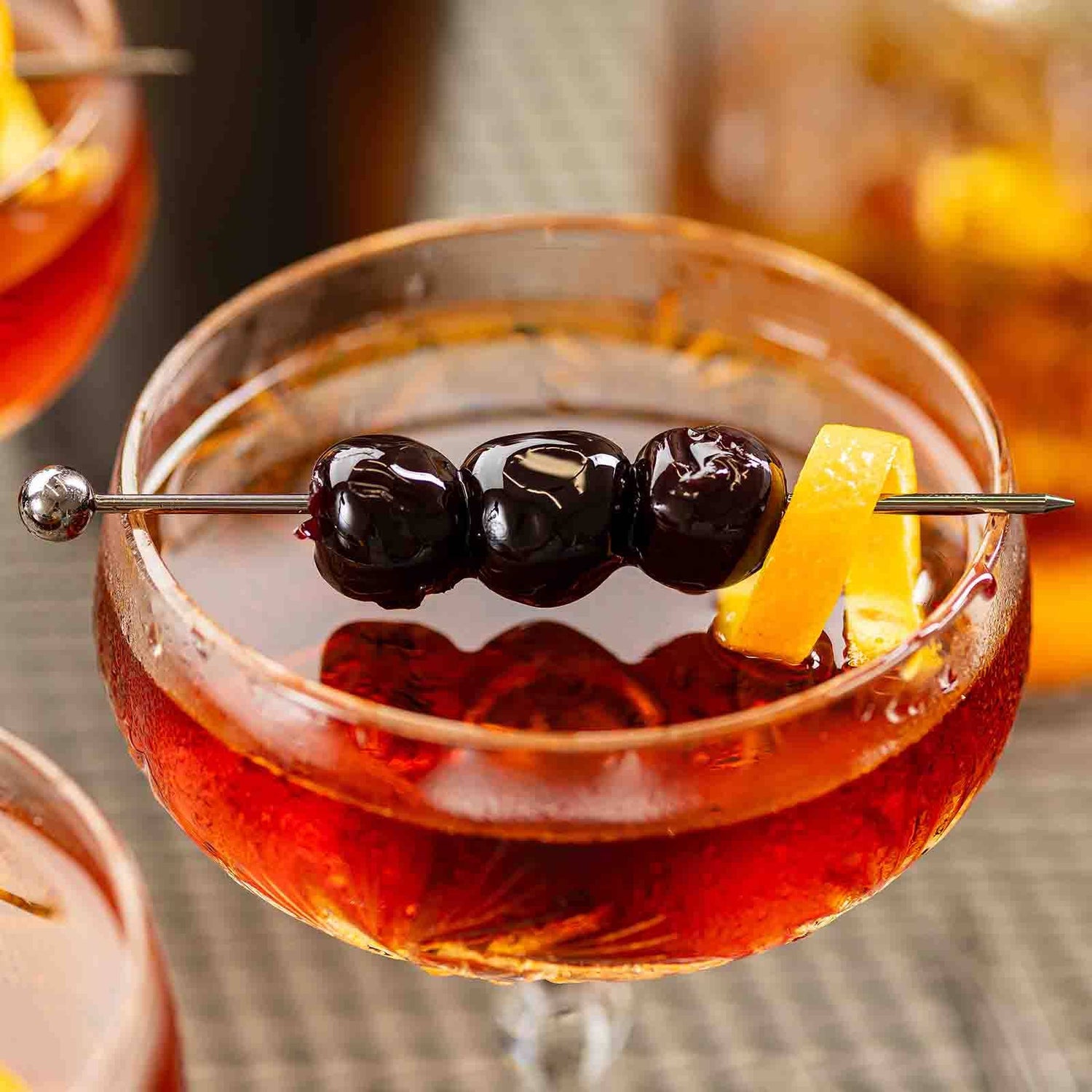 Cocktail with a blueberry and lemon peel garnish in a glass skewed by the Gunmetal Cocktail Pick.