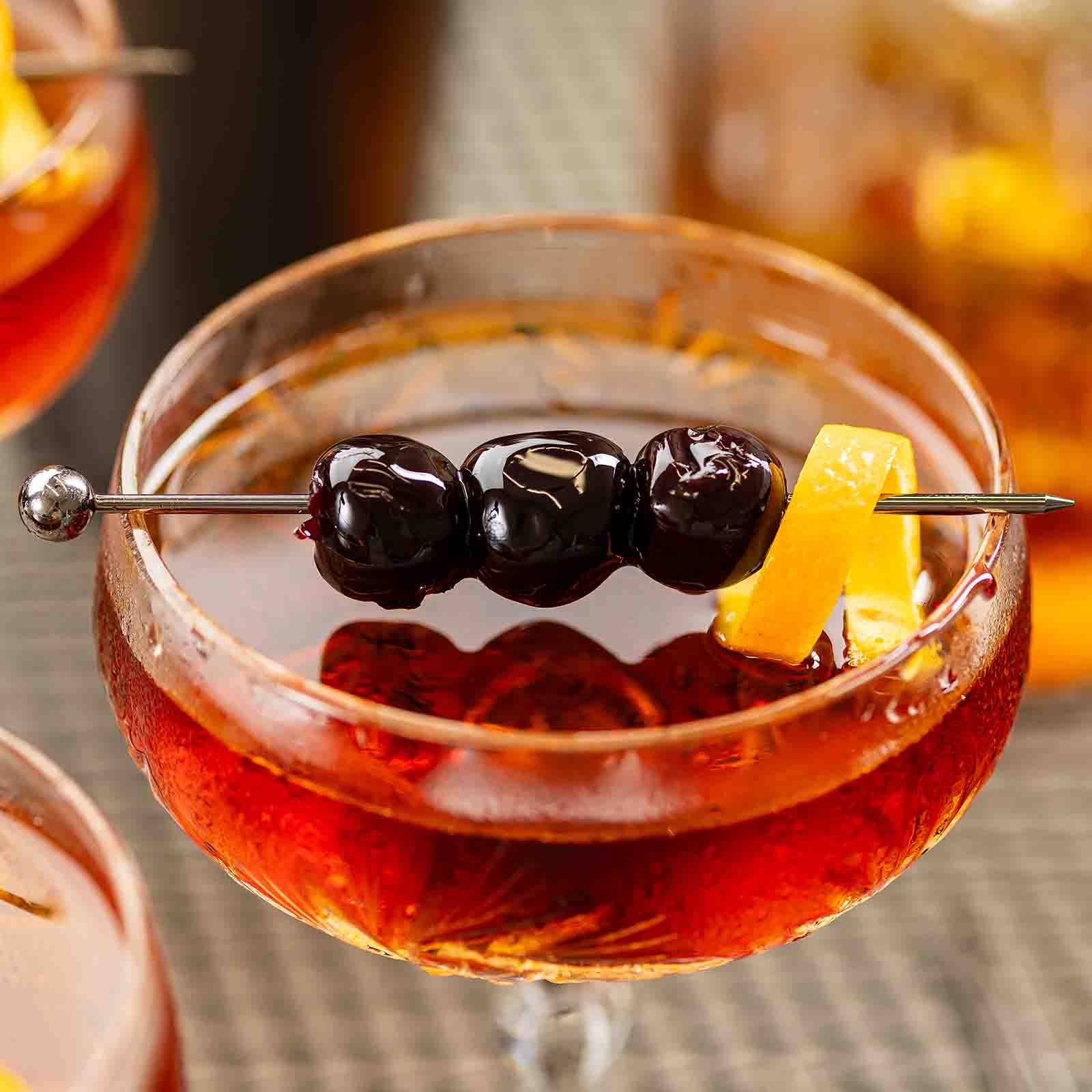 Cocktail with a blueberry and lemon peel garnish in a glass skewed by the Gunmetal Cocktail Pick.