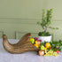 A decorative gold cornucopia-style bowl overflowing with fruit, placed on a marble surface in front of a potted plant against a sage green paneled wall.