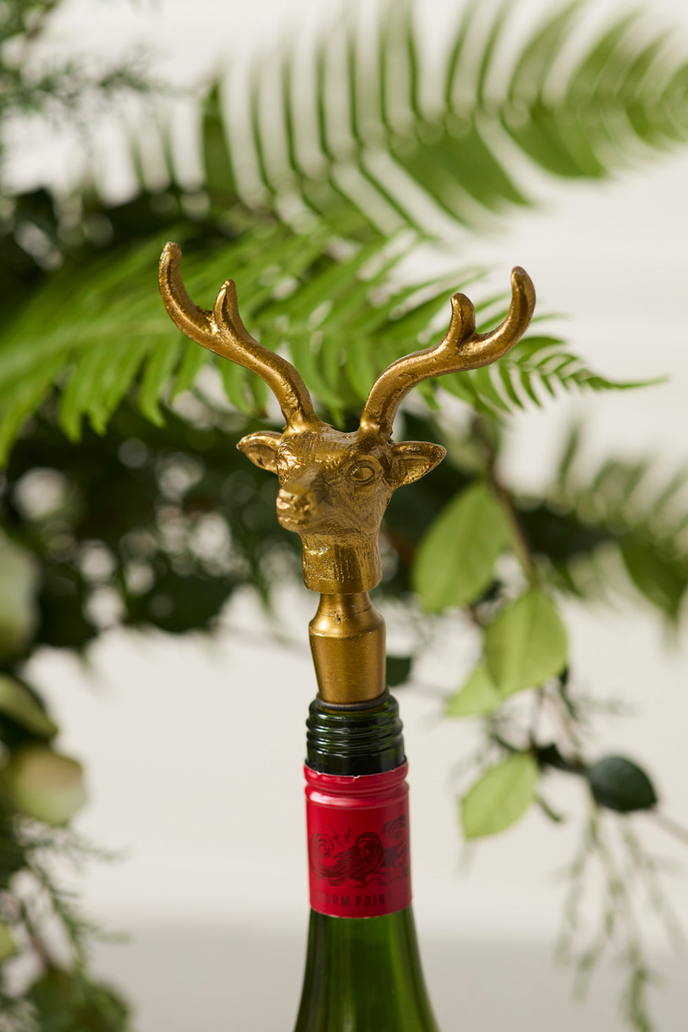 Gold deer head bottle stopper on a wine bottle with a blurred green leafy background.