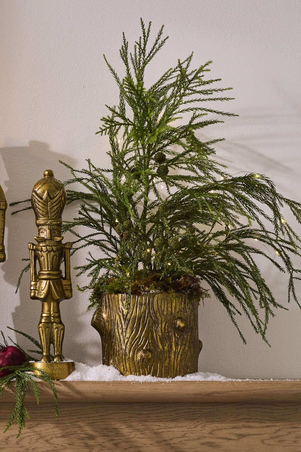 Decorative plant in a gold pot with a nutcracker and red berry on a wooden surface.