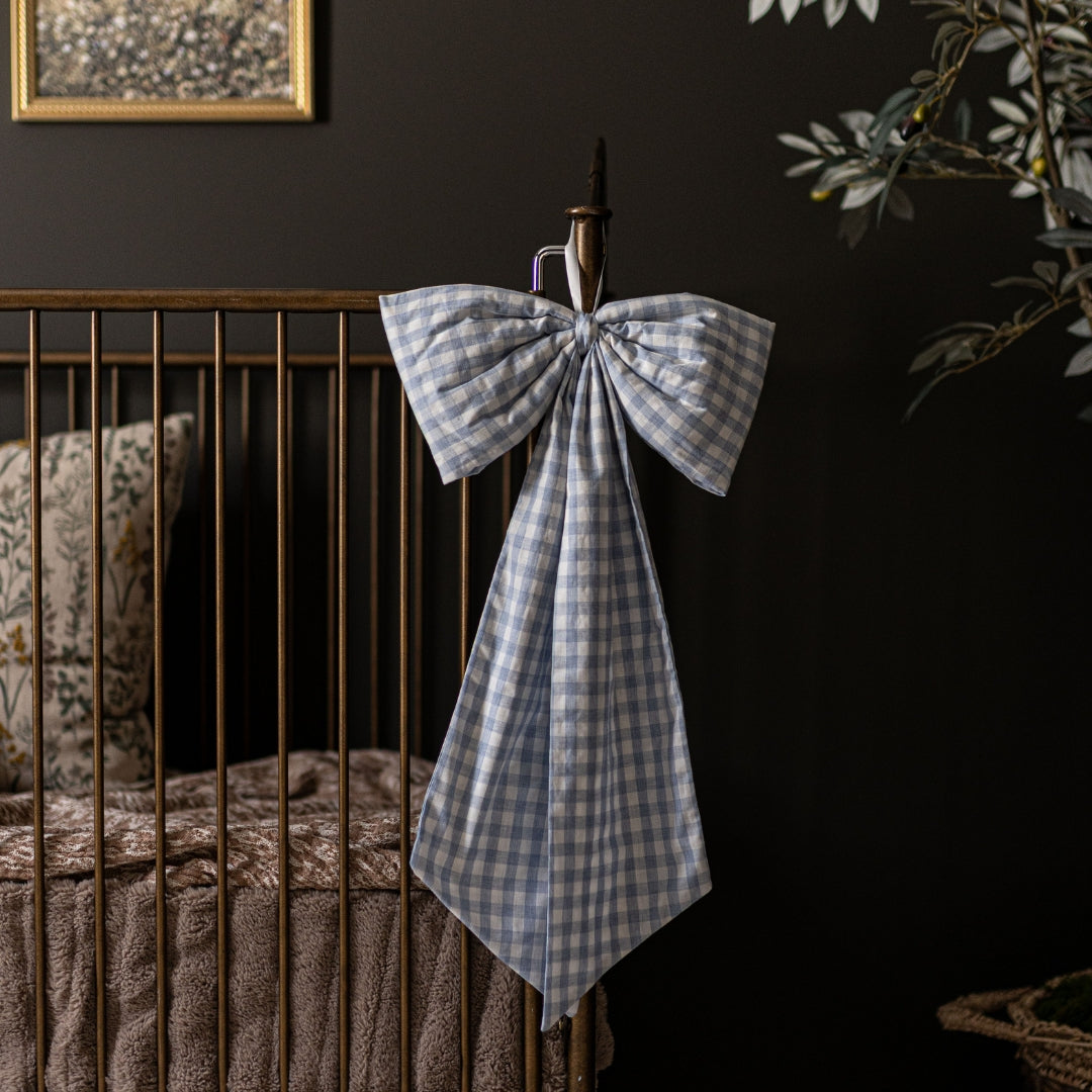 Crib with a decorative blue checkered bow against a dark wall.