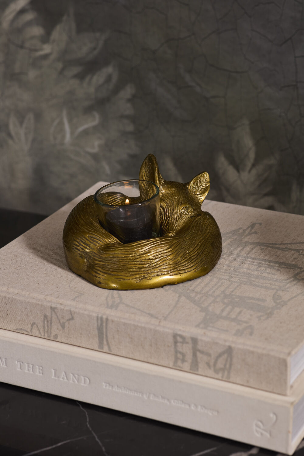 Gold fox-shaped candle holder on a book with a dark background.
