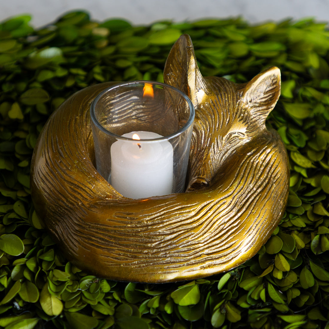Gold fox-shaped candle holder with a lit candle on a green leafy background