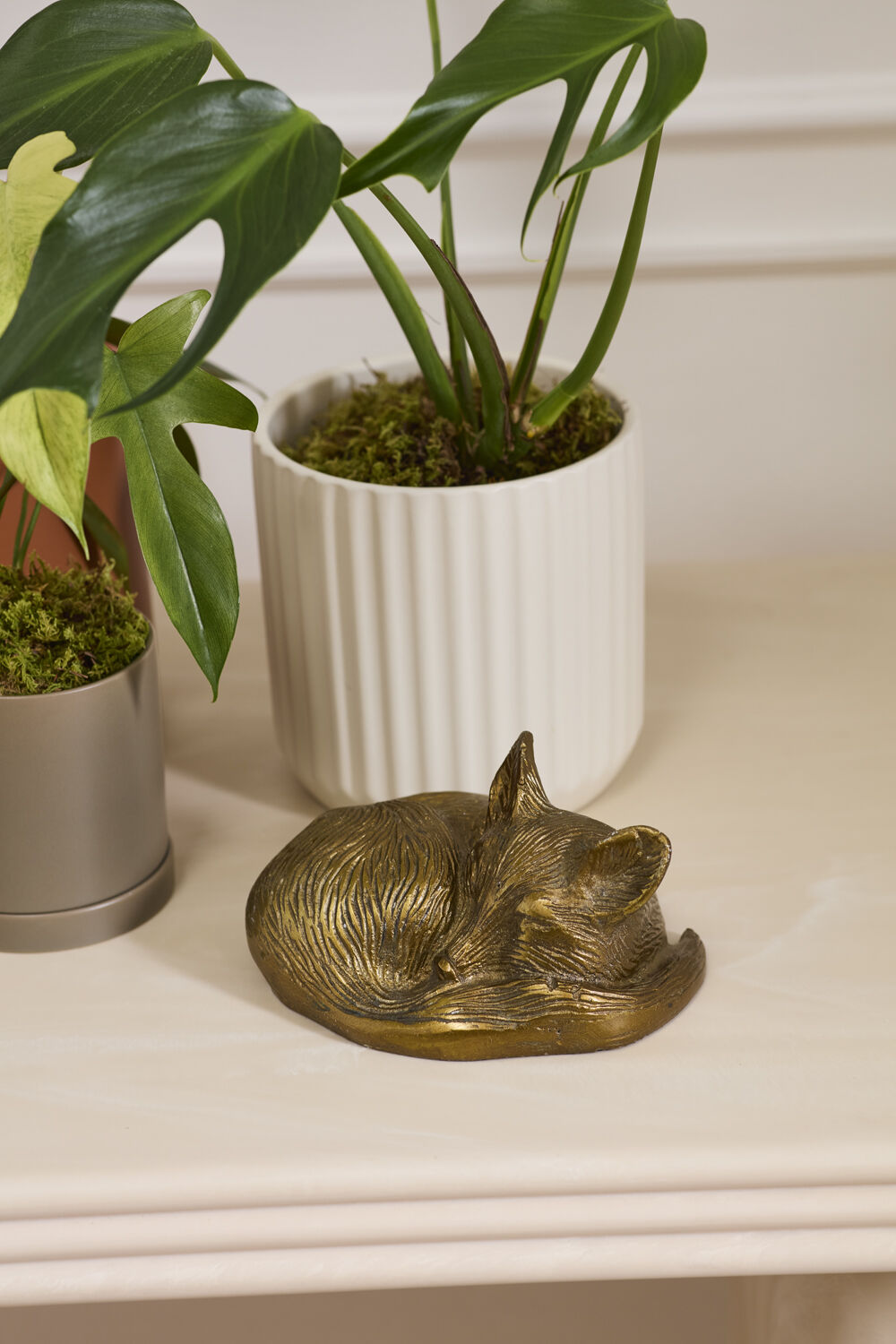 Bronze fox figurine on a surface with potted plants in the background.