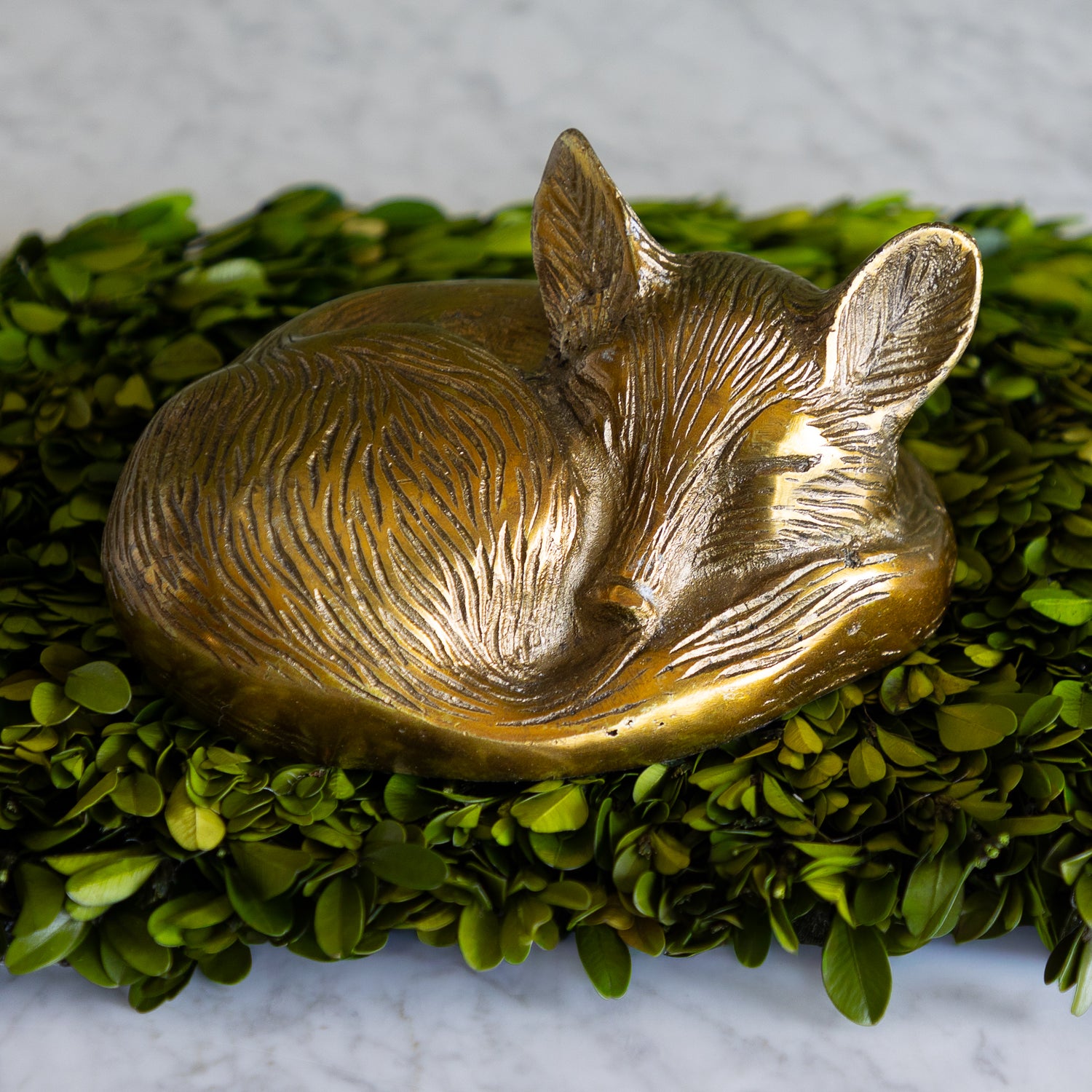 Bronze fox figurine on a bed of green leaves.