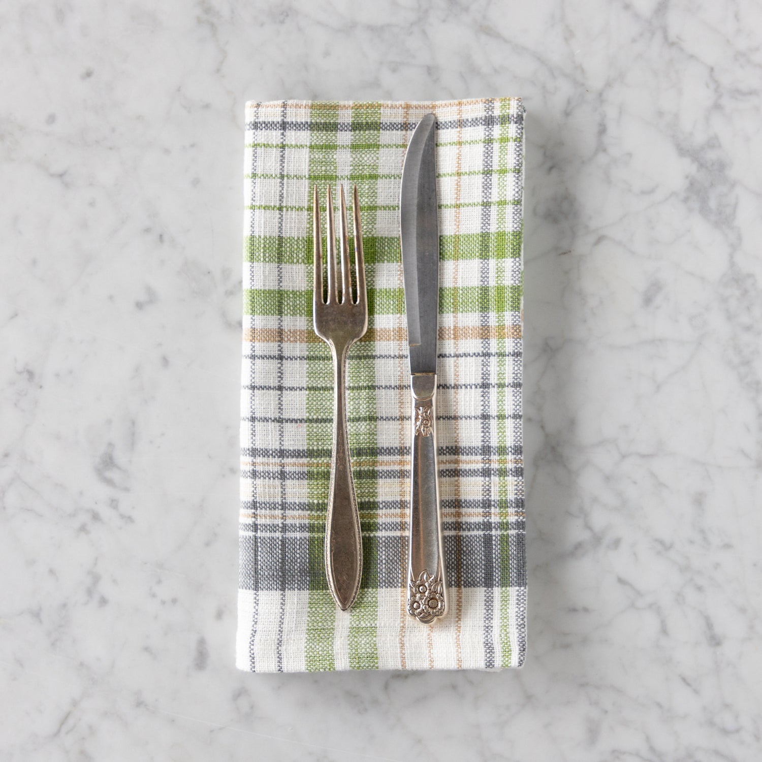 Folded plaid napkin with a fork and knife on a marble surface.