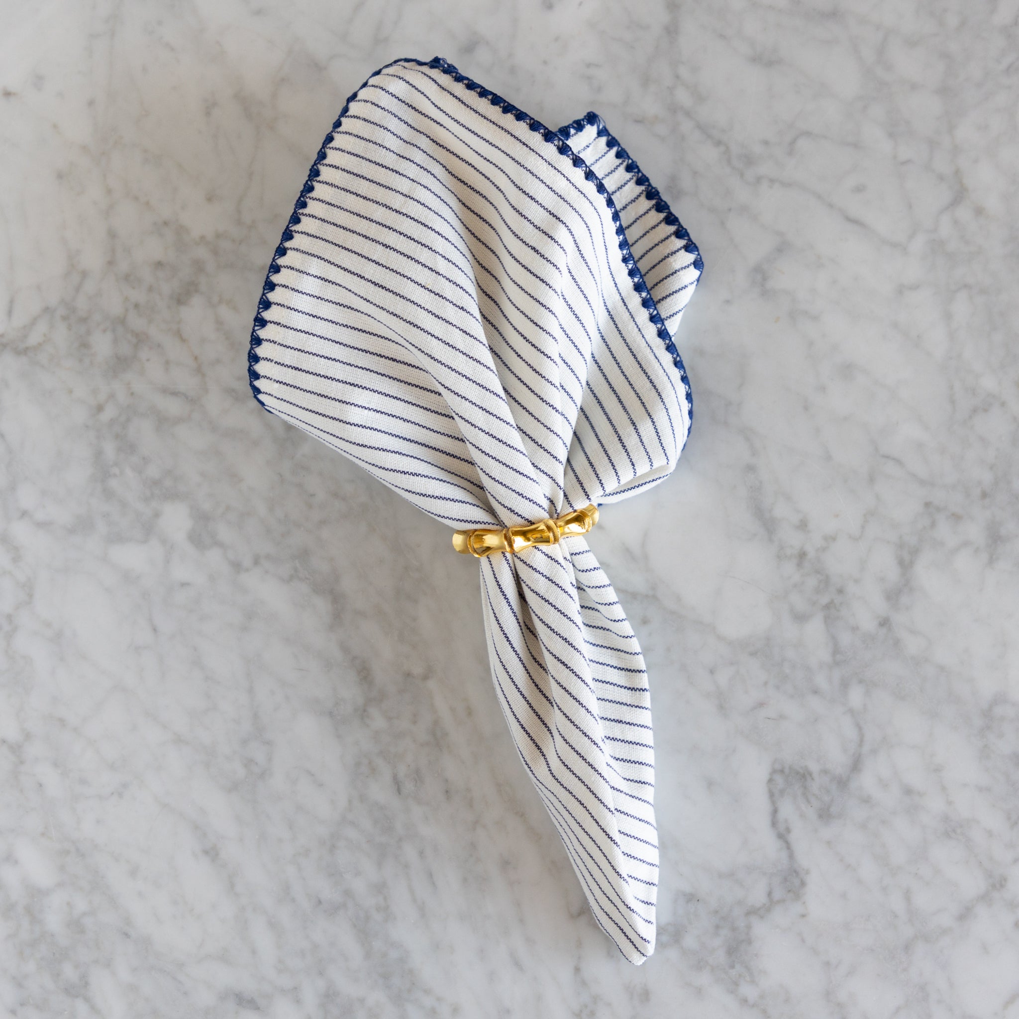 Striped napkin with a gold ring on a marble surface.