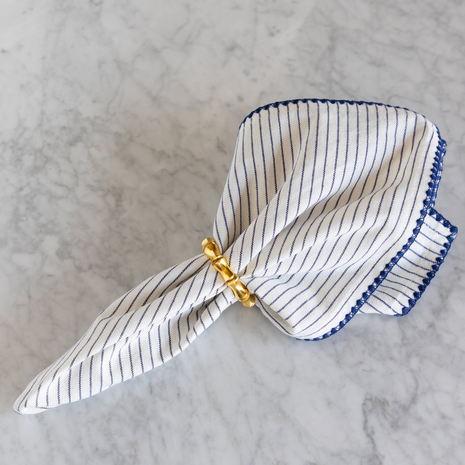 Striped napkin with a gold napkin ring on a marble background.