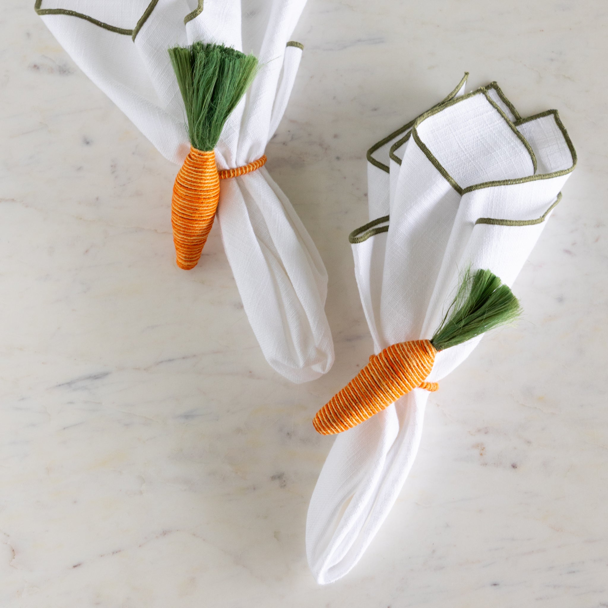 Carrot-shaped napkin rings on white napkins with a marble background.