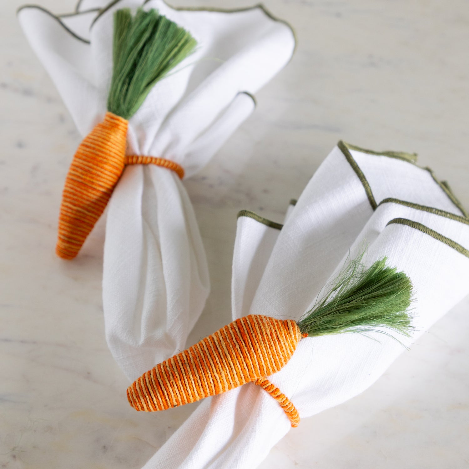 Carrot-shaped napkin rings on white napkins with a marble background.