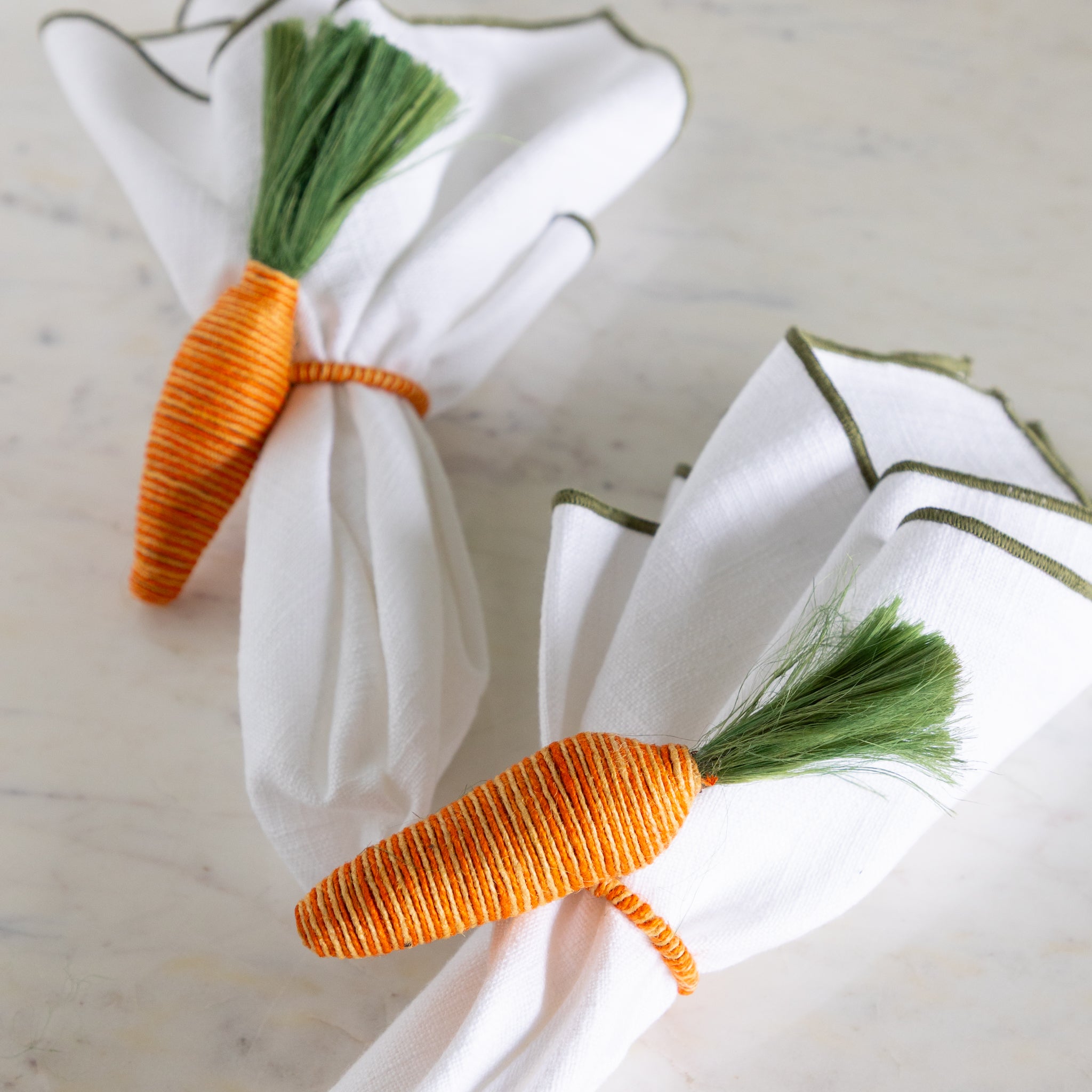 Carrot-shaped napkin rings on white napkins with a marble background.