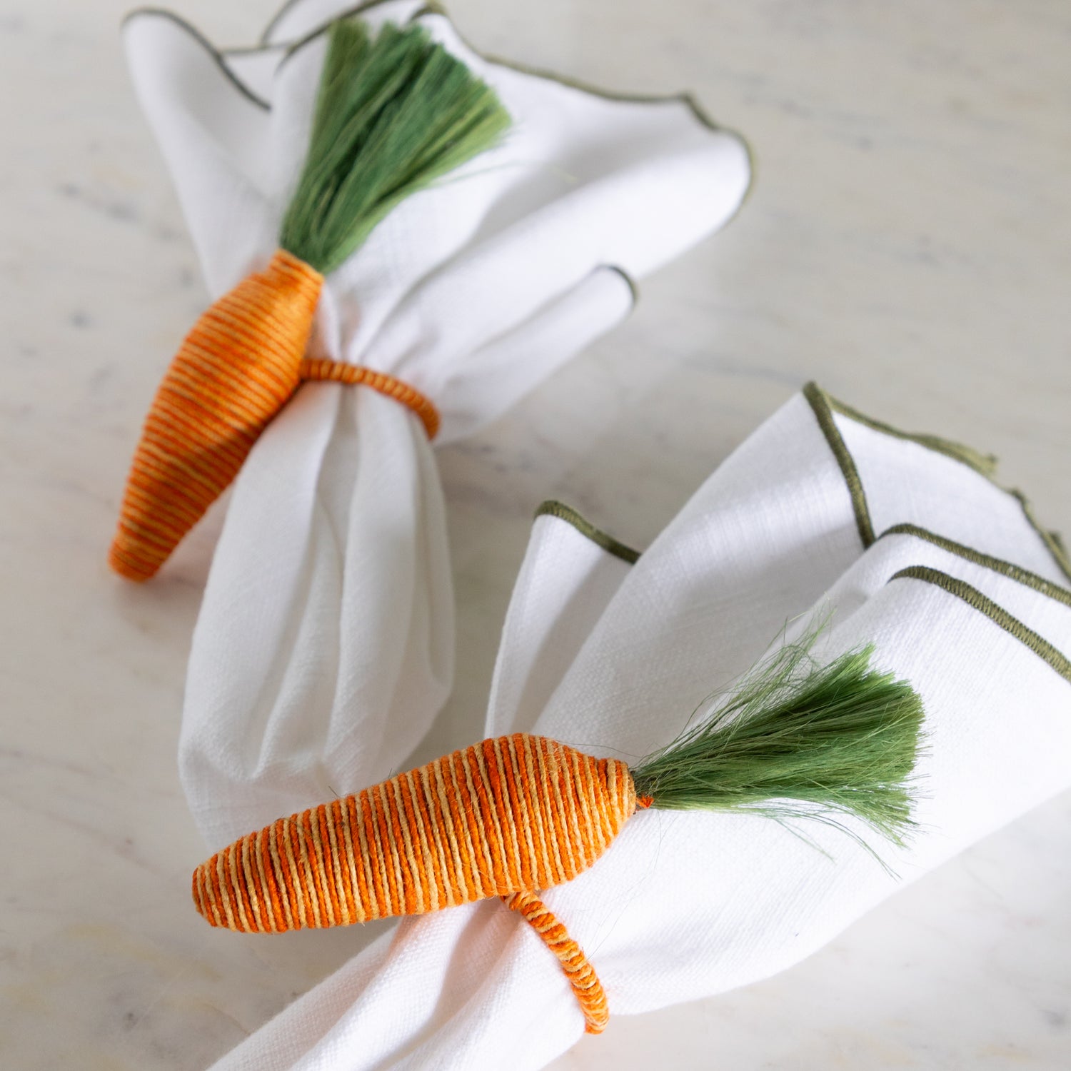 Carrot-shaped napkin rings on white napkins with a marble background.