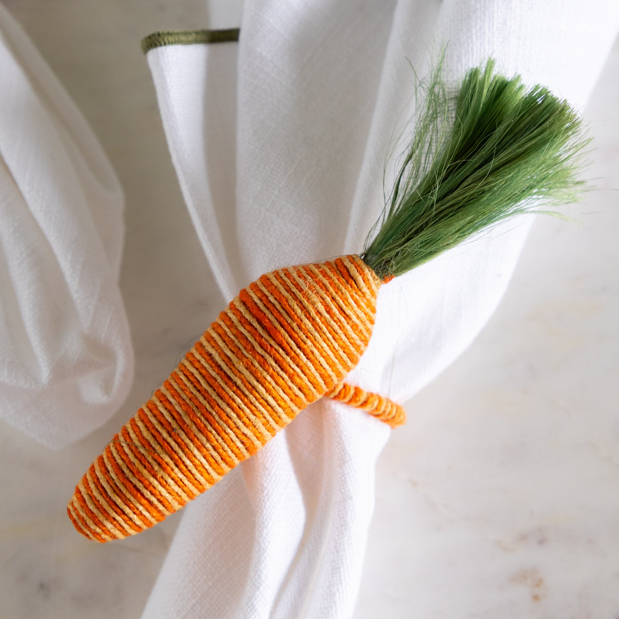 Carrot-shaped napkin ring on a white napkin with a marble background.
