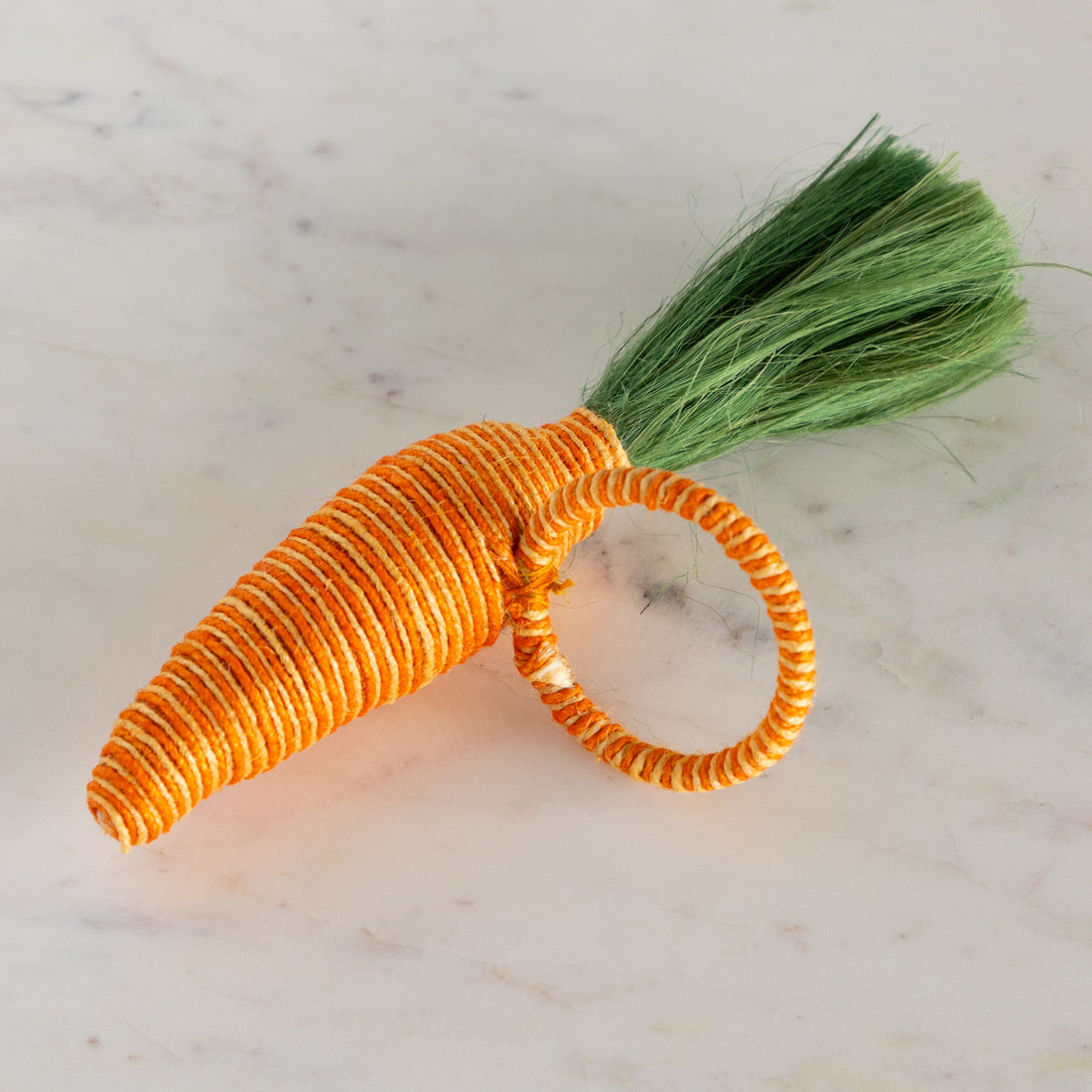 Carrot-shaped napkin ring with a green stem on a marble surface.