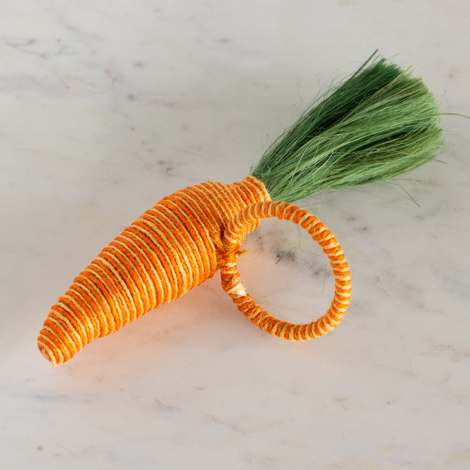 Carrot-shaped napkin ring with a green stem on a marble surface.