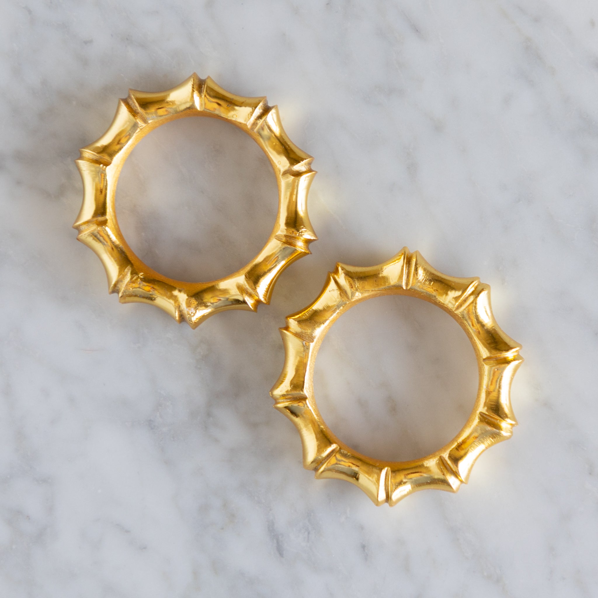 Two gold bamboo style napkin rings on a marble surface.
