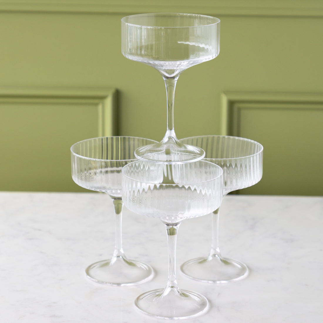 Four Fluted Textured Coupe Glasses; three on the table and one stacked on top.