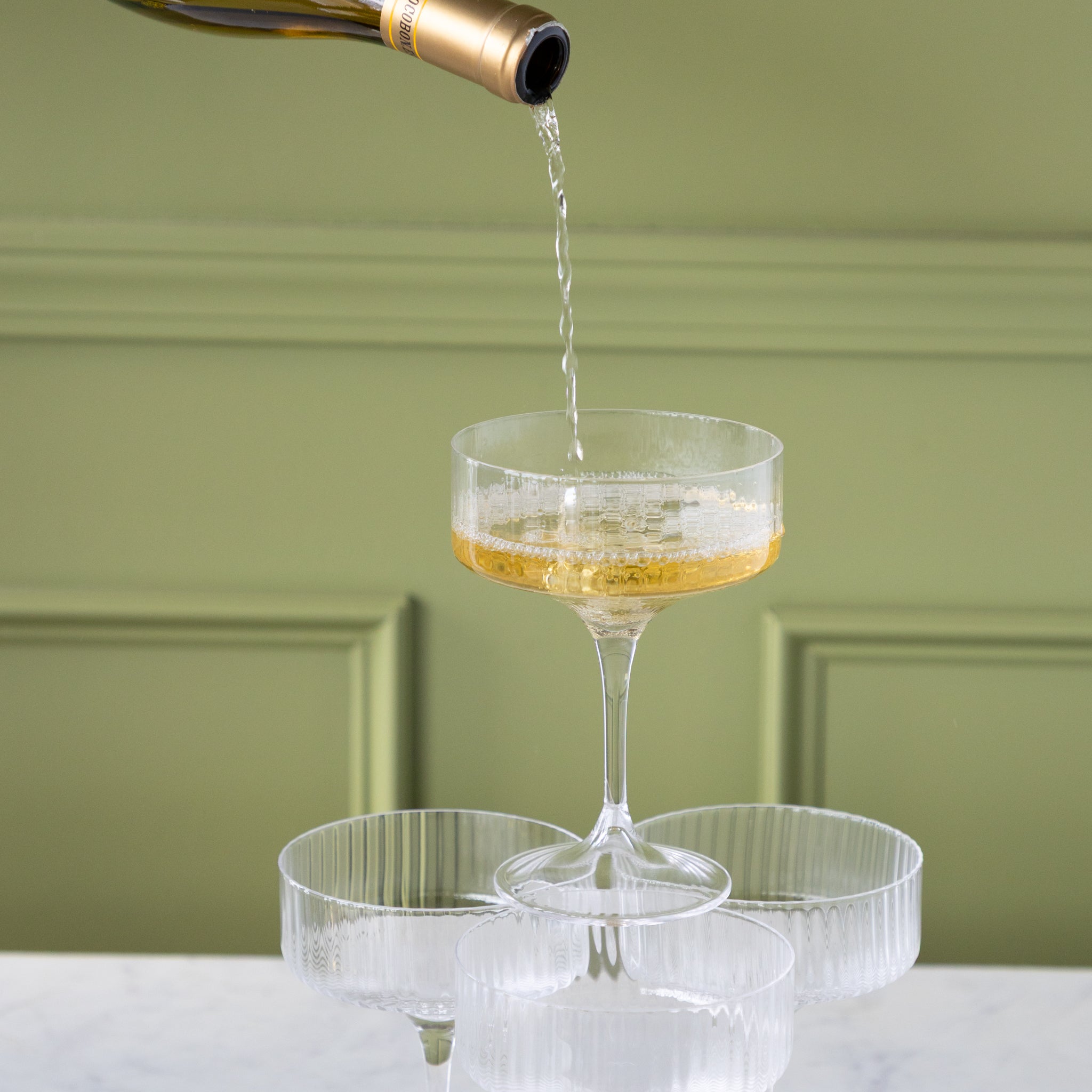 Champagne being poured into a Flute Textured Coupe Glass stacked on other glasses.